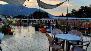 Una terraza con mesas y sillas, plantas en macetas y montañas al fondo.