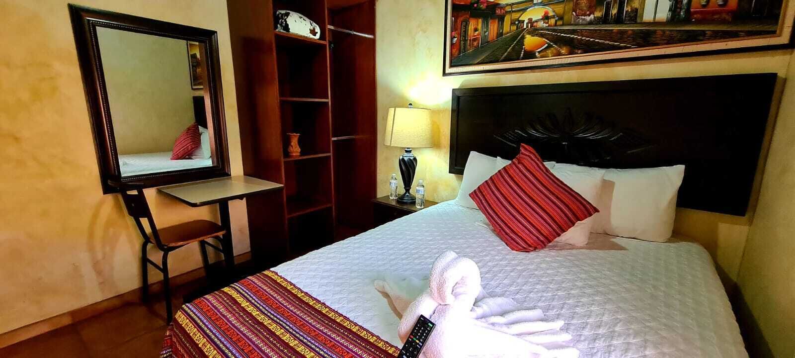 Ein Hotelzimmer mit Bett, Schreibtisch, Spiegel, Kleiderschrank und einem Gemälde an der Wand.
