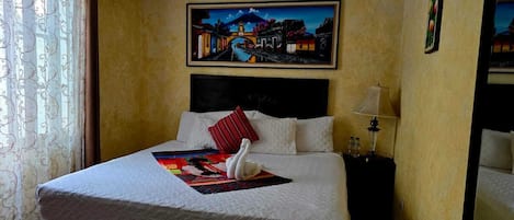 Habitación de hotel con una cama grande, una mesita de noche, una lámpara y un cuadro de un paisaje urbano en la pared.