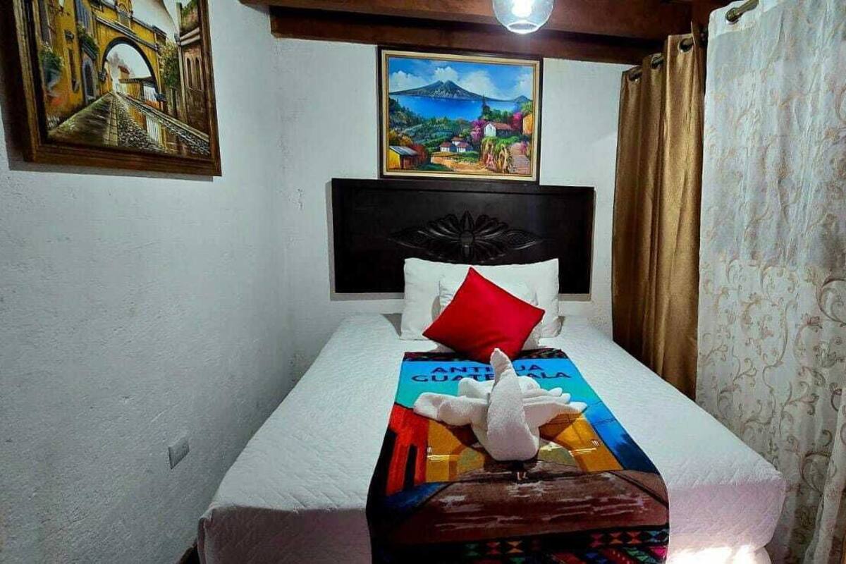 A hotel room with a bed, a headboard, a pillow, a blanket, a wall painting, and curtains.