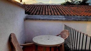 A balcony with a round table and two wooden chairs, a tiled roof, and a metal railing.