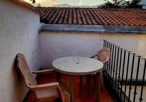 A balcony with a round table and two wooden chairs, a tiled roof, and a metal railing. - Hotel Real Antigua (Antigua Guatemala)