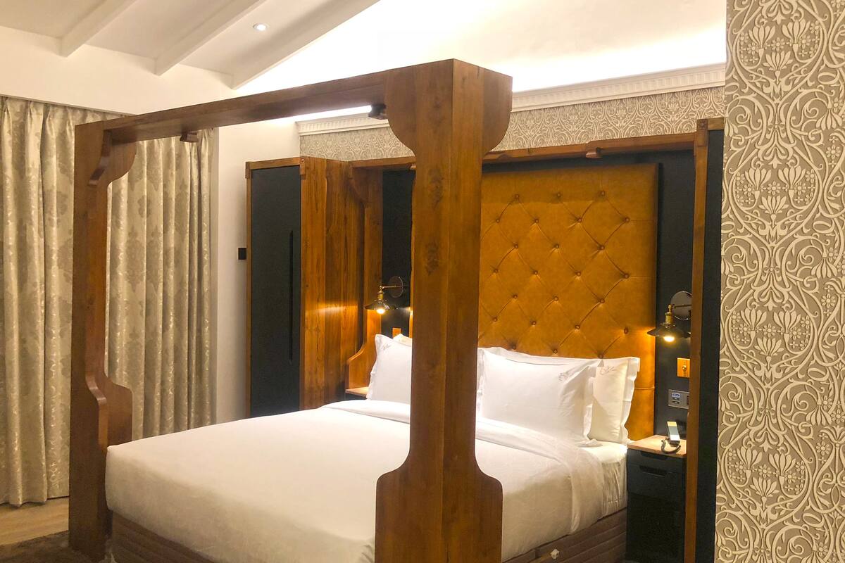 Ein Bett mit Baldachin, ein gebürstetes Kopfende, ein Nachttisch mit Lampe und eine wandbeschichtete Tapete.