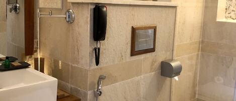 A modern bathroom with a white sink, toilet, and shower. There are towels on a shelf and a phone mounted on the wall.