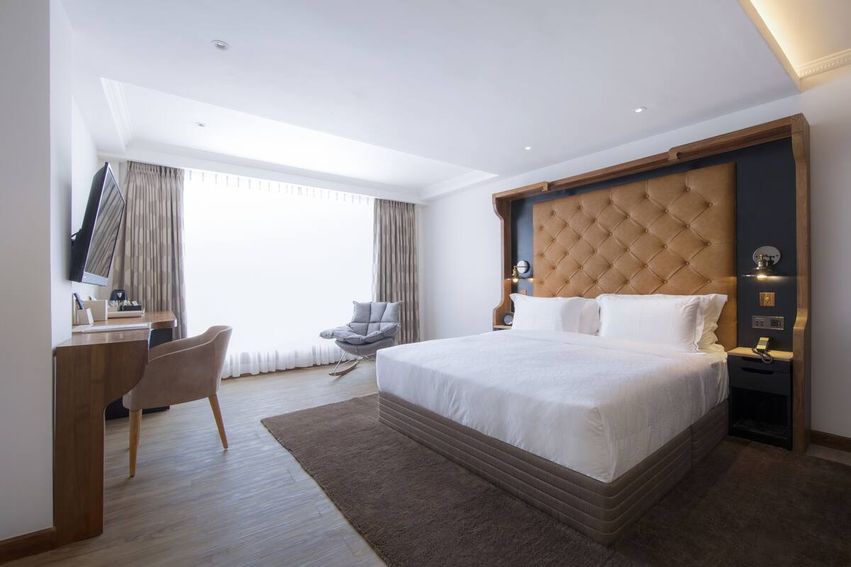 Ein modernes Hotelzimmer mit einem großen Bett, einem Schreibtisch, einem Sessel und einem Fernseher.