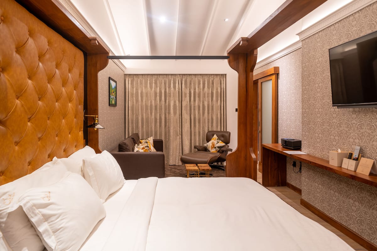 Ein Hotelzimmer mit einem großen Bett, einer Sitzecke mit Sofa und Sesseln, einem Fernseher und einem Holzregal mit Annehmlichkeiten.