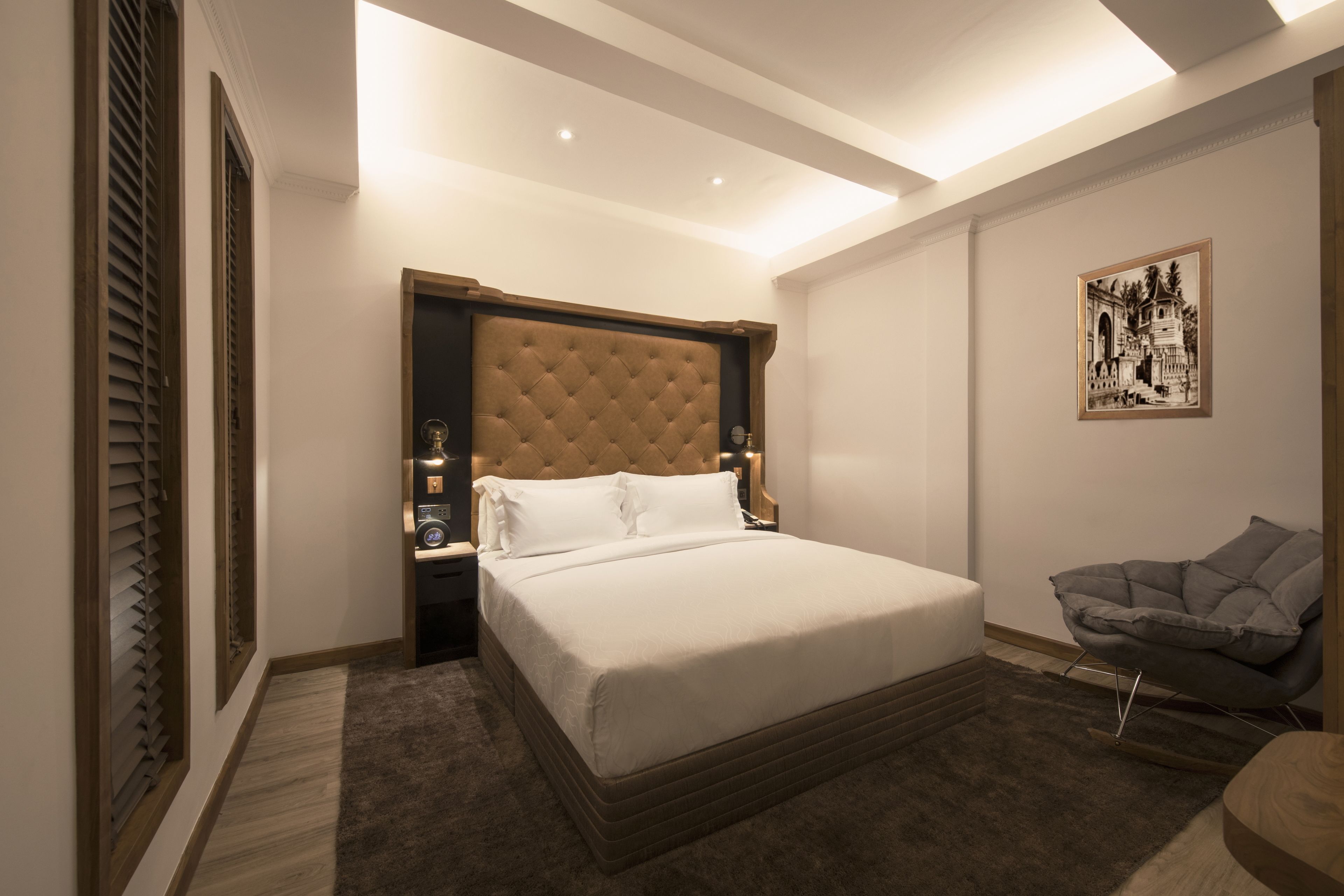Une chambre à coucher avec un grand lit, une table de chevet, une chaise et un tableau encadré au mur.
