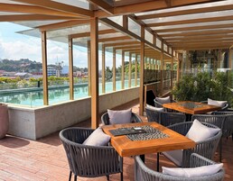 Un área de estar al aire libre con mesas y sillas, con vistas a una piscina y al paisaje urbano.