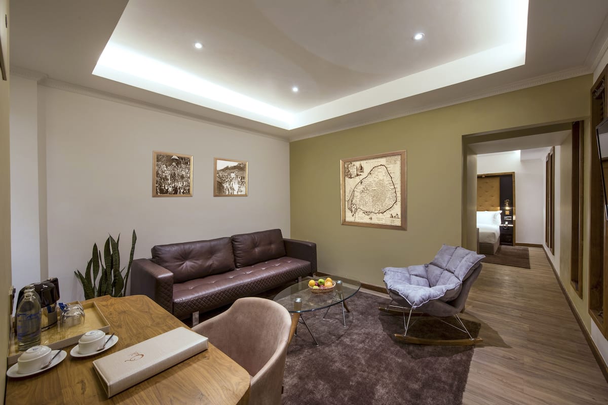 Ein modernes Wohnzimmer mit einer Ledersofa, einem Glastisch, einem gepolsterten Sessel und einem Esstisch mit Tellern und einer Glas-Kanne.