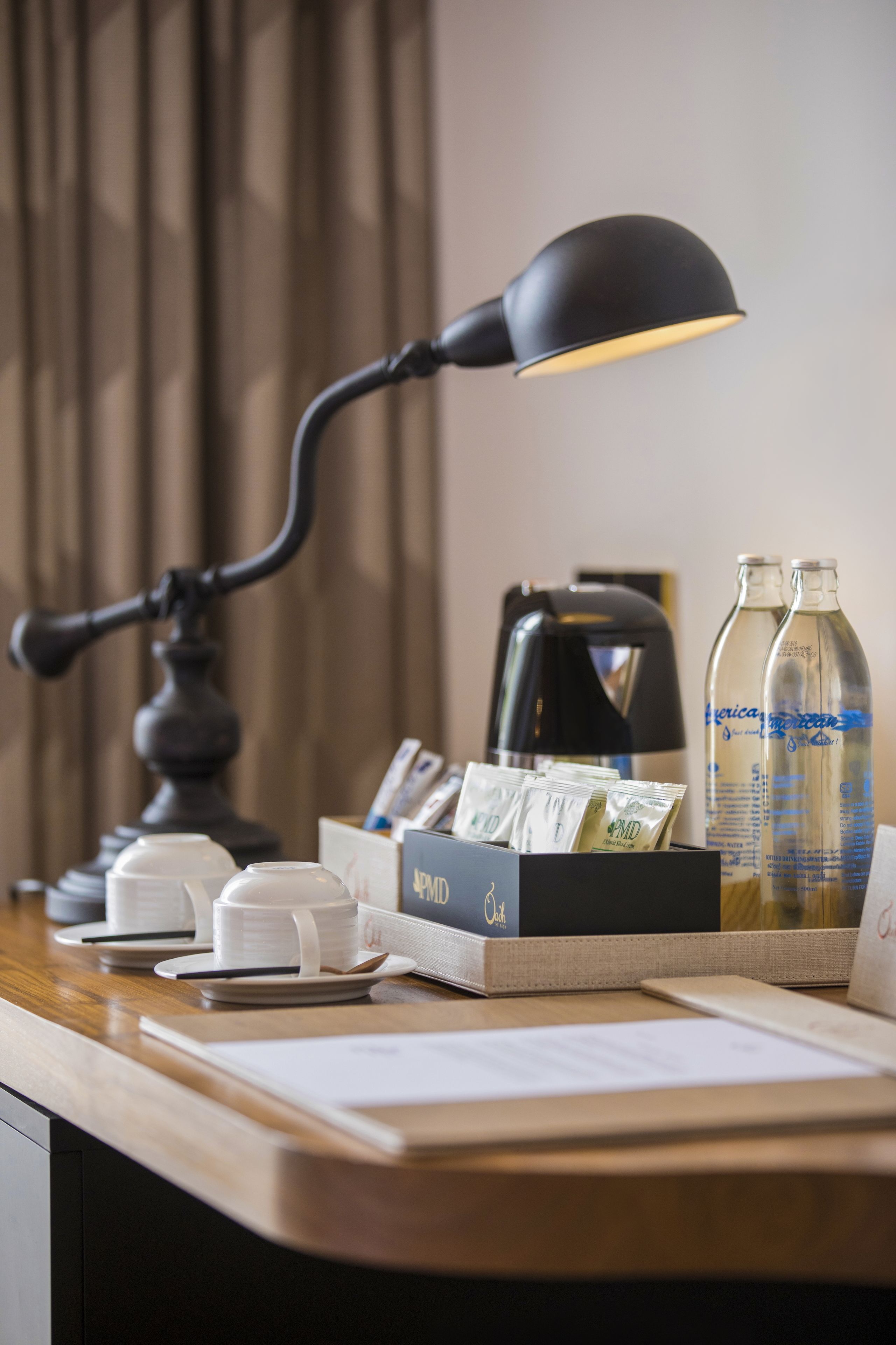 A hotel desk with a lamp, coffee maker, water bottles, and a box of tissues.