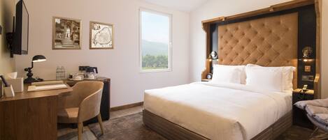 A hotel room with a large bed, a desk with a chair, a desk lamp, and two framed pictures on the wall.
