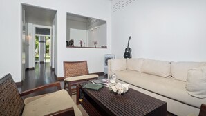 A living room with a sofa, a wooden coffee table, a guitar, and a mirror on the wall. - Ban Mok Talay Beachfront Villa (Koh Samui)