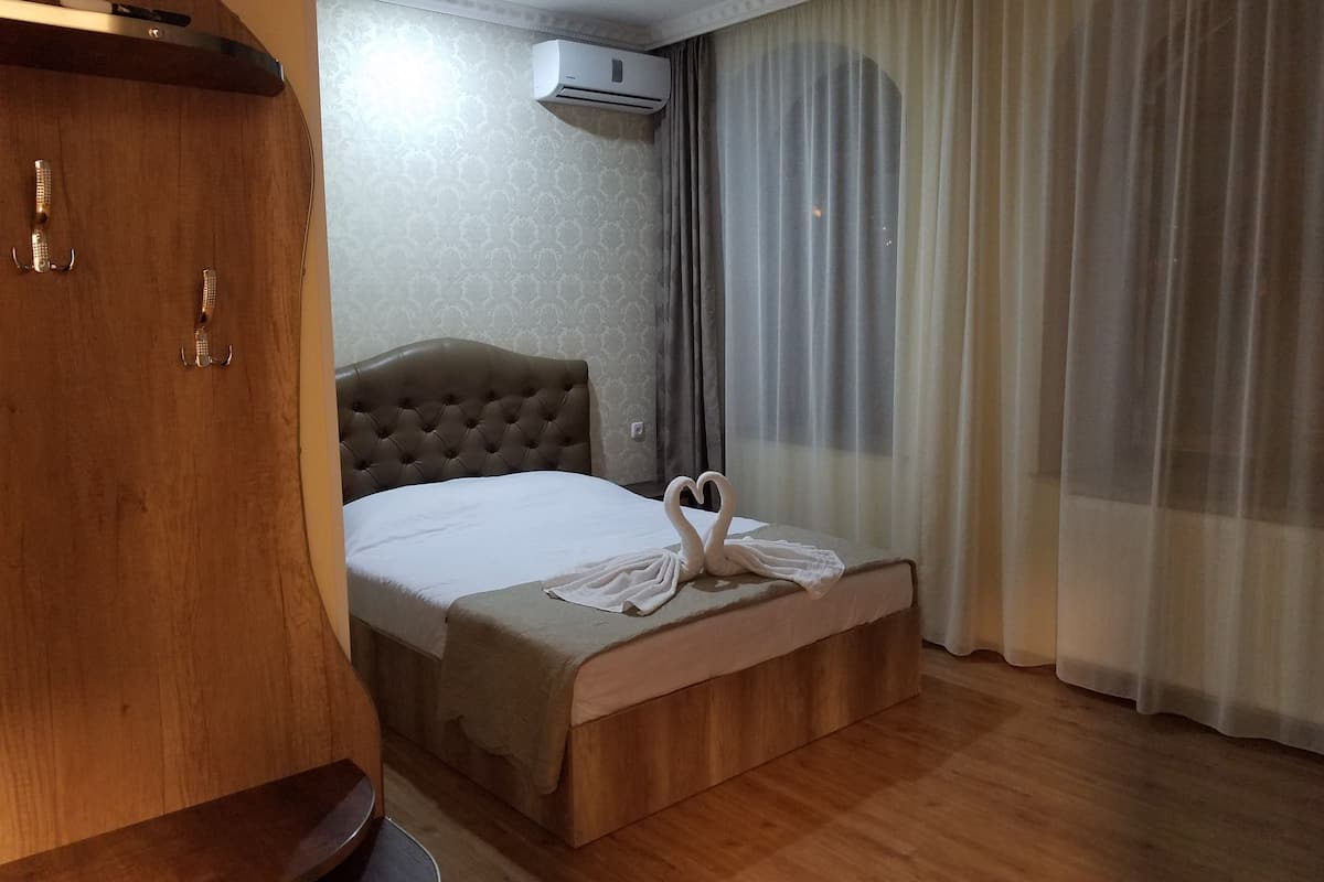 Ein Hotelzimmer mit einem Holzschrank, einem Bett mit einem herzförmigen Handtuch und einem Fenster mit transparenten Vorhängen.