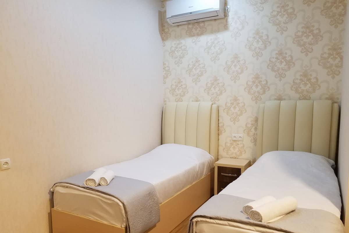 Ein kleines, sauberes Zimmer mit zwei Einzelbetten, einem Nachttisch und einer Wand-Klimaanlage.