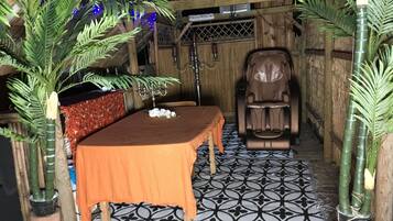 A massage chair in a room with a patterned floor, a table with a blanket, and decorative plants.