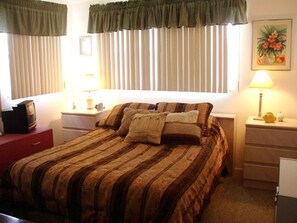 Un dormitorio con una cama, dos mesitas de noche, una lámpara, un cuadro y un televisor.