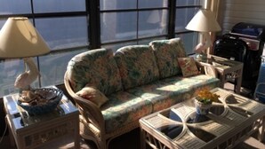 A room with a floral sofa, two lamps, a wicker table, and a view through large windows. - Venice Villas on the Beach (Venice)