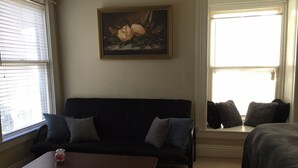 Una habitación con un sofá negro, una mesa de centro de madera y un cuadro de flores en la pared.