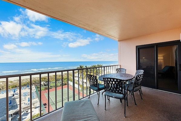 Un balcon avec une table et des chaises, donnant sur une plage et l’océan.