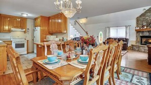 Une cuisine spacieuse avec des meubles en bois, un coin repas agrémenté d’un lustre et une cheminée dans le salon.