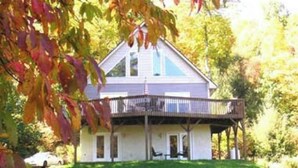 Une maison à deux étages avec un balcon, entourée d’arbres et dotée d’une allée.