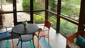 Un invernadero con mesa y sillas, ventanas amplias y vistas a un jardín.