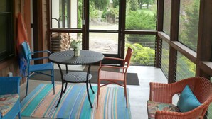 Un patio cubierto con mobiliario de mimbre, una mesa y vistas a un jardín y árboles.