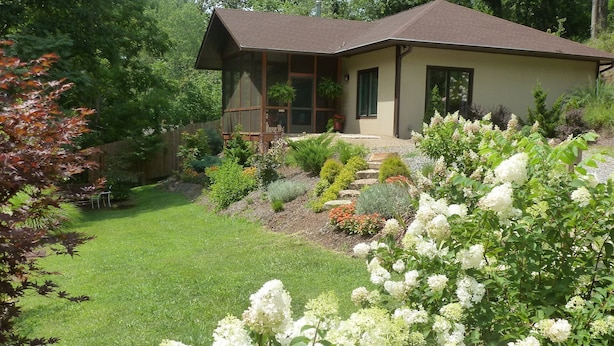 Una casa con un jardín cuidado, una terraza de madera y césped.