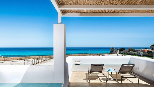 Ein Balkon mit zwei Stühlen und einem Tisch mit Blick auf Strand und Meer.