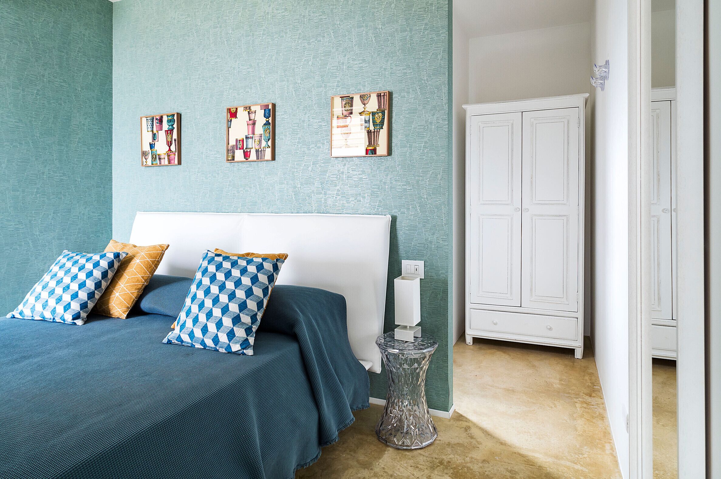 A bedroom with a bed, blue and white patterned pillows, a small side table, and a white wardrobe.