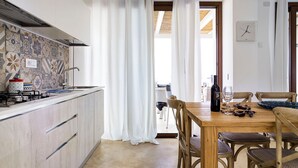 Eine moderne Küche mit gefliestem Rücksprung, einem Holzesstisch mit Stühlen und Blick ins Freie durch ein Fenster.