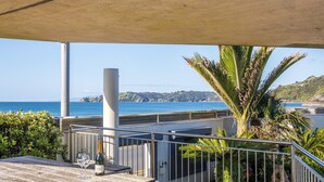 A terrace with a view of the sea, a palm tree, and a bottle of champagne. - Absolute beachfront position on Waiheke Island. (Onetangi)