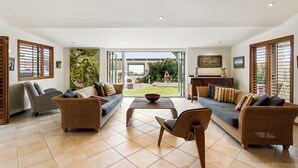 A spacious living room with a sofa, chairs, a coffee table, and a view of the outdoors. - Absolute beachfront position on Waiheke Island. (Onetangi)