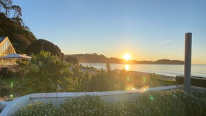 A waterfront property with a view of the sunset over the water, a wooden deck, and a garden area. - Absolute beachfront position on Waiheke Island. (Onetangi)