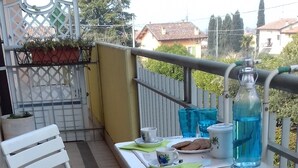 Un balcón con una silla blanca, una mesita con una bandeja y una botella azul.