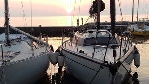 Dos veleros amarrados en un puerto deportivo, con aguas tranquilas y un atardecer al fondo.