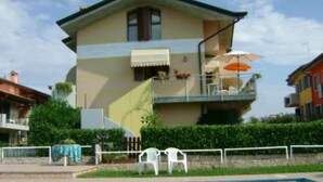 Una casa de dos pisos con un balcón, una piscina en primer plano y un cielo despejado.