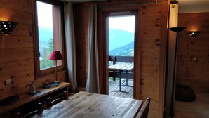 A wooden cabin with a dining table and chairs, a red lamp, and a view of mountains through a door. - Valmorel Duplex, 3 bedrooms, 6-8 pers - Skis at your feet, in the heart of the resort (Les Avanchers-Valmorel)