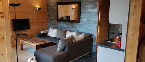 Un salon chaleureux avec un canapé gris, une table basse en bois et un téléviseur à écran plat fixé au mur.
