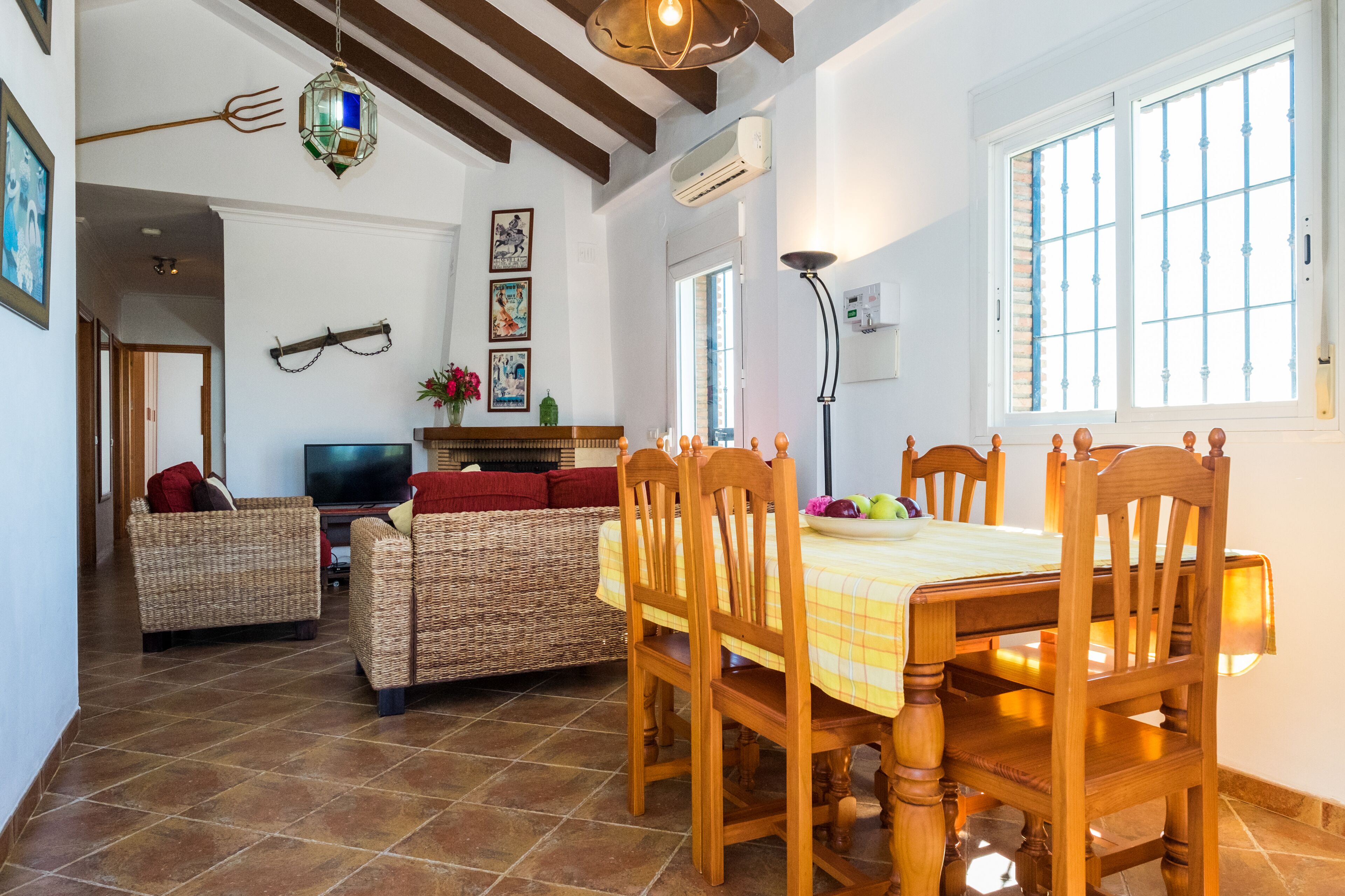 A dining area with a wooden table and chairs, a wicker sofa, and a television in the background.