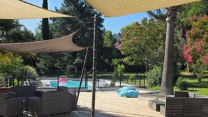 Zona junto a la piscina con mobiliario exterior, una piscina y una pérgola que proporciona sombra.