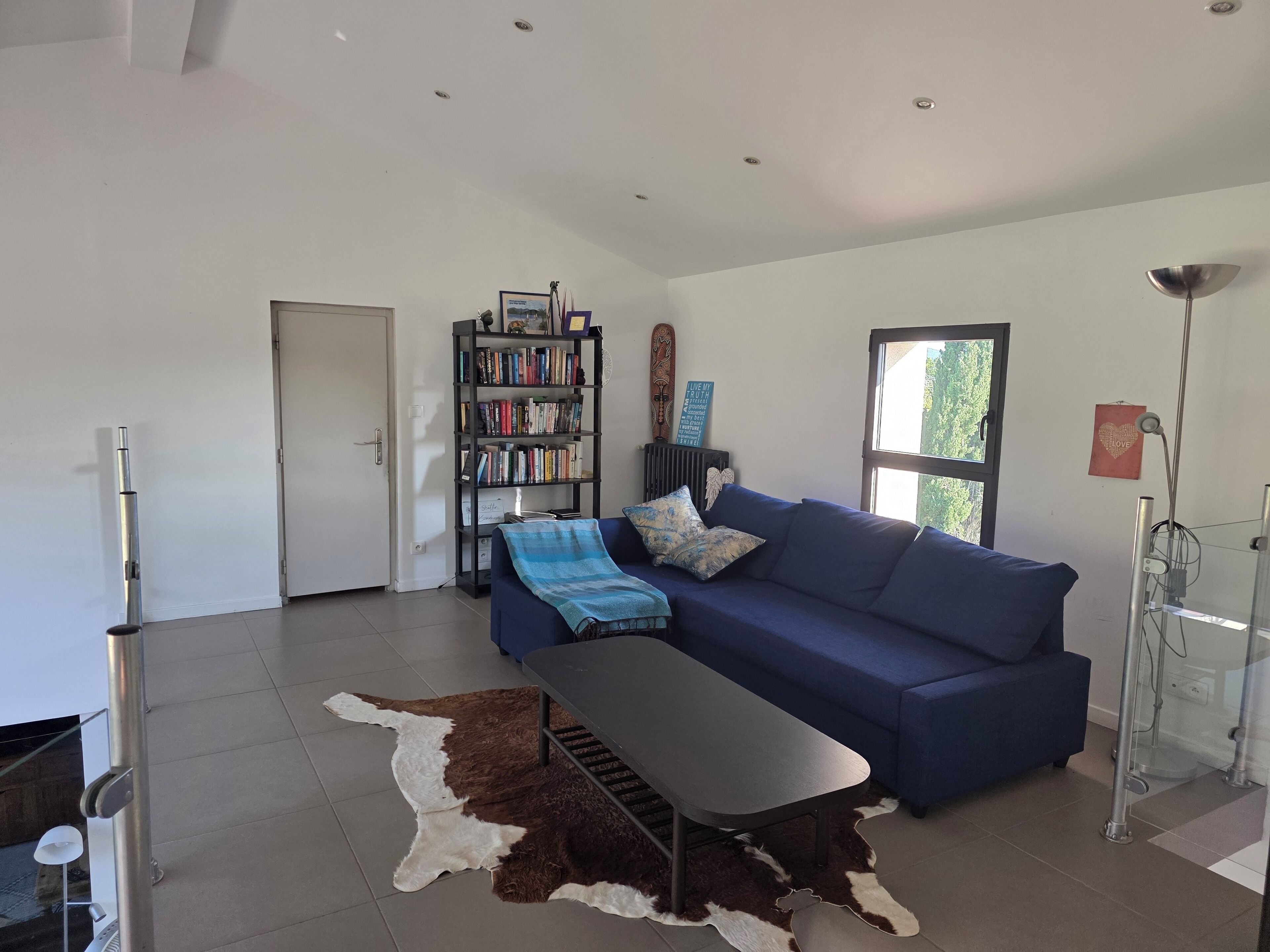 Un salon moderne avec un canapé bleu, une table basse, une bibliothèque et une cabine de douche en verre.