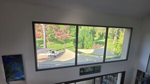 Habitación con un amplio ventanal que da a un jardín ajardinado con árboles y un sendero.