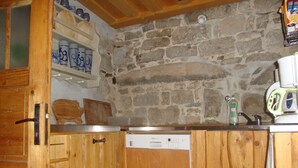 A kitchen with wooden cabinets, a Bosch dishwasher, and a stone wall.