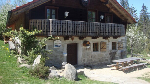 A rustic wooden building with a balcony, stone walls, and a wooden door.