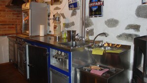 A kitchen with a stainless steel sink, a refrigerator, and a coffee machine. There are signs on the wall and a wooden ceiling.