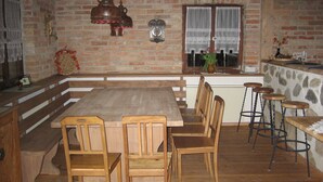 A cozy kitchen with a wooden table and chairs, a brick wall, and a window with curtains.
