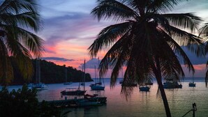 A coastal scene with boats docked at a marina, surrounded by palm trees and a sunset sky. - Apartment, near beach, view of the sunset, 2 bedrooms, sleeps 6 (Les Anses d'Arlet)