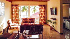 A room with a wooden ceiling, a dining table with chairs, a TV mounted on the wall, and a potted plant. - Apartment, near beach, view of the sunset, 2 bedrooms, sleeps 6 (Les Anses d'Arlet)