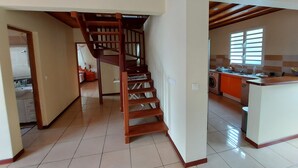 A spacious kitchen with a central island, wooden staircase, and a view of the adjacent living area. - Apartment, near beach, view of the sunset, 2 bedrooms, sleeps 6 (Les Anses d'Arlet)
